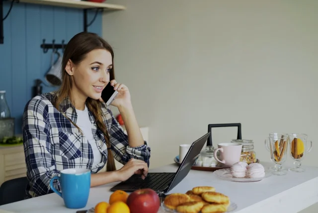 woman at a kitchen table on the phone to her bank after a scam text