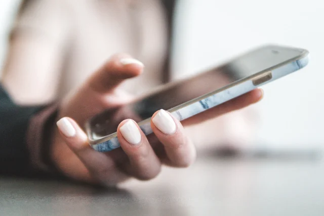 close-up of a hand holding a smartphone ready to forward a scam text to 7726