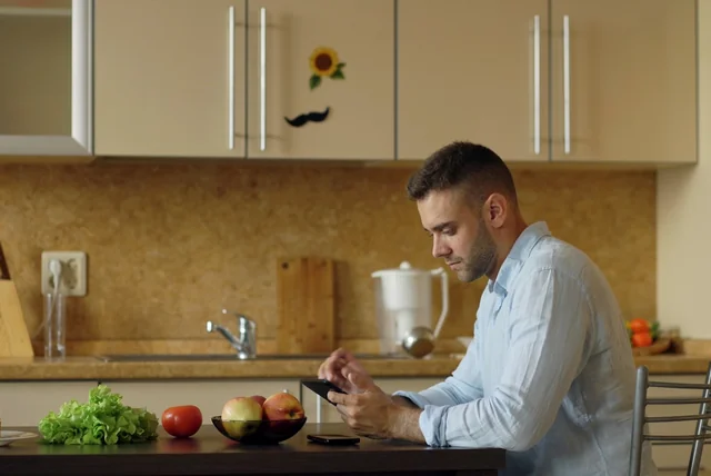 bank transfer scam refund – man at his kitchen table checking his banking app after being scammed