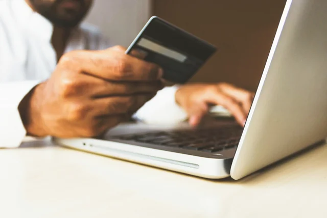 Shopper with a bank card at a laptop pausing to check if a website is legit before buying