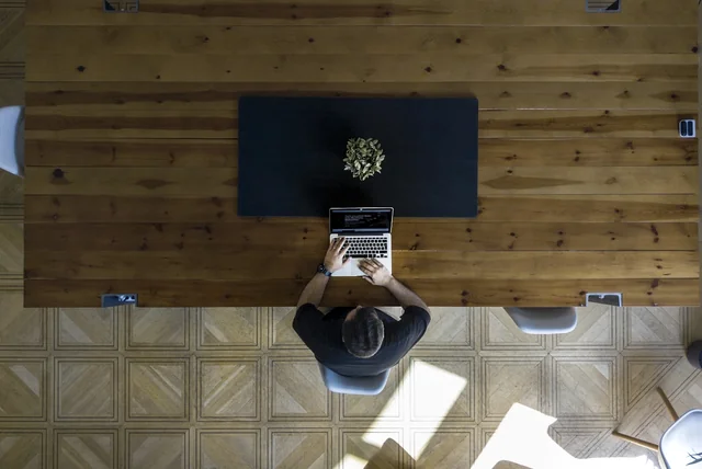 person at a wooden table stepping back from their device after clicking a scam link