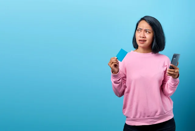 worried woman holding her bank card and phone after paying a fake parking fine
