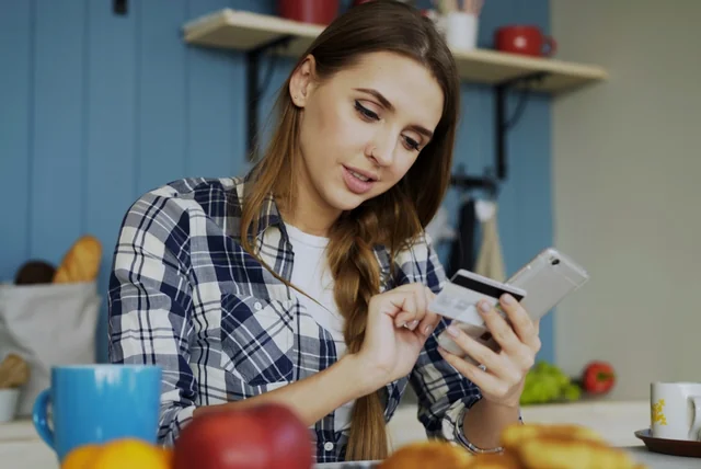 Woman holding her bank card and phone to call her bank after tapping a scam text link