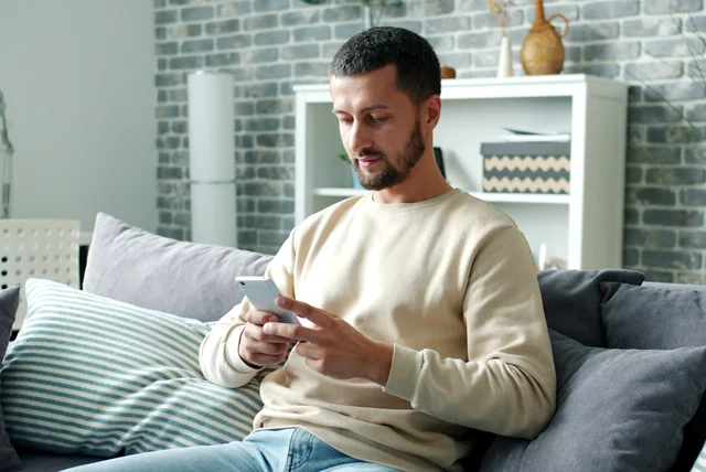 Man calmly reading a genuine HMRC text message with no links on his phone at home