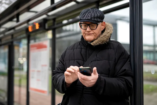 Older man in a winter coat checking a suspicious winter fuel payment text on his phone