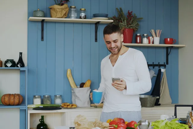 hmrc text scam – man reading a suspicious text message on his phone over morning tea in the kitchen