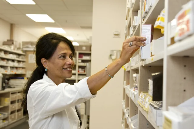 Pharmacist picking a medicine box from a shelf for an NHS App repeat prescription