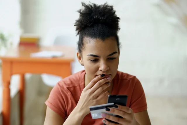 worried woman holding a bank card and phone, ready to call 159 instead of trusting a bank email
