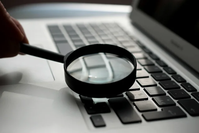 magnifying glass over a laptop keyboard while checking a suspicious web address