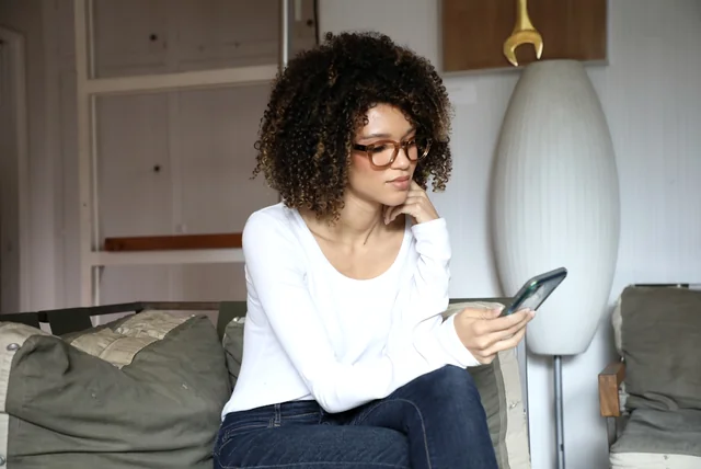 woman reading a suspicious Royal Mail delivery fee text on her phone at home